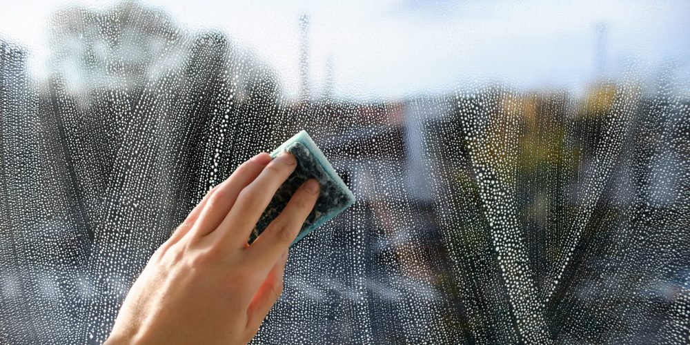 Glass cleaner with a sponge for cleaning windows. The person uses a sponge to apply detergent to the window.